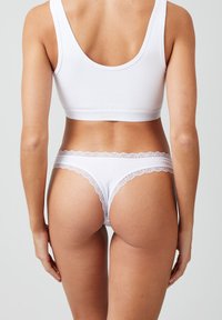 Witte lingerie set bestaande uit een aansluitende bralette met een brede band en bijpassende string met een kanten rand langs de tailleband. Zachte stofstructuur.