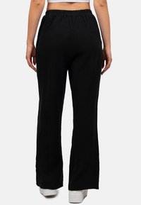 Zwarte, rekbare, lichtgewicht broek gemaakt van een textuur met een gekreukelde stof. Heeft een wijde pijp en een elastische tailleband voor extra comfort.