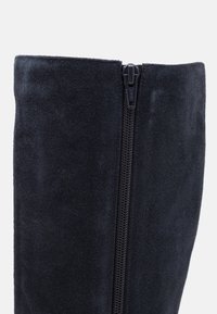 Gros plan sur la tige d'une botte en daim noir avec une fermeture éclair YKK noire centrale courant verticalement.