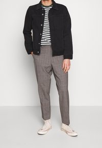 Černá džínová bunda, pruhované tričko v bílé a zelené barvě a kostkované kalhoty v šedých tónech, doplněné béžovými teniskami.