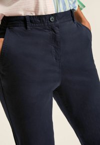 Granatowe spodnie wykonane z gładkiego materiału, z zapięciem na guzik, bocznymi kieszeniami oraz dopasowanym krojem. Minimalne detale przeszyć widoczne.