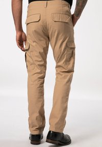 Beige Cargo-Hosen aus strukturiertem Stoff, mit zwei Gesäßtaschen und Seitentaschen, kombiniert mit schwarzen Schuhen, von hinten betrachtet.