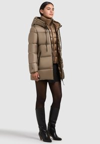 Khaki pufferjack met een capuchon; heeft een glanzende afwerking, ritszakken en verstelbare trekkoorden; gelaagd over een bijpassend lichter topje.