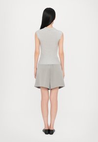 Top senza maniche grigio a maglia con colletto alto, abbinato a pantaloni corti grigi leggeri. Le scarpe slip-on nere completano l'outfit.