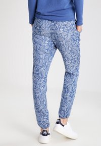 Pantalons jogger à motif paisley bleu en tissu doux, avec une taille élastique et des poignets élastiques, associés à des baskets blanches.