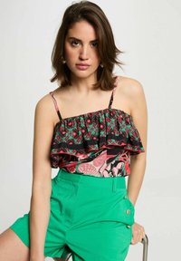 Top volant in tessuto floreale nero, rosso e verde, abbinato a pantaloni corti verdi con dettagli in bottone dorato. Tessuto leggero.