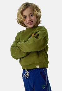 Sweat-shirt en coton vert avec un col rond et des poignets côtelés, porté avec un pantalon de jogging bleu présentant des rayures verticales et une poche accentuée.