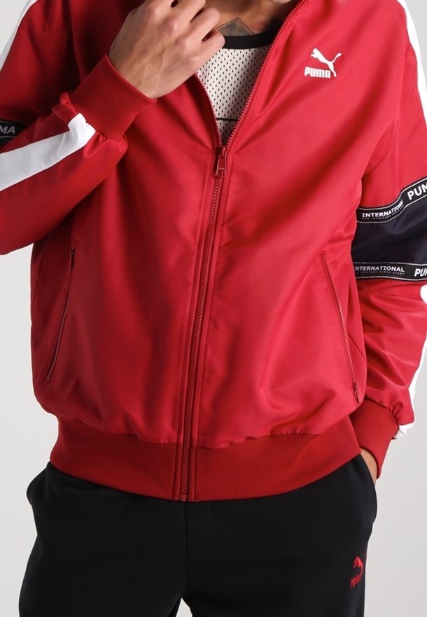 Chaqueta bomber roja con rayas blancas en las mangas, logo de la marca en el pecho, cierre de cremallera, puños y dobladillo acanalados, fabricada con tejido suave.