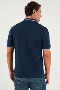 Polo majica u mornarsko plavoj boji s mekim teksturom, s kontrastnim bijelim obrubom na ovratniku i rukavima. Kratki rukavi i opušteni kroj.