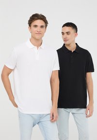 Due camicie polo a maniche corte in esposizione: una bianca con colletto classico e bottoni, l'altra nera con un design simile.