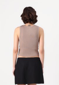 Top cu coarne, fără mâneci, de culoare maro deschis, având un croi scurt și un gât rotund. Asortat cu o fustă neagră, care prezintă un design simplu.