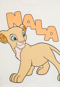 Light-colored T-shirt featuring a cartoon lion cub with green eyes and a beige body, accompanied by the orange text "NALA."