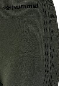 Leggings deportivos de color verde oscuro con cintura acanalada, logo negro, patrón texturizado a lo largo del costado con perforaciones y formas geométricas.