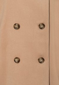 Dubbelgeknoopt jasje van zacht beige stof, met vier ronde bruine knopen. Gladde textuur met een getailleerde pasvorm en strakke lijnen.