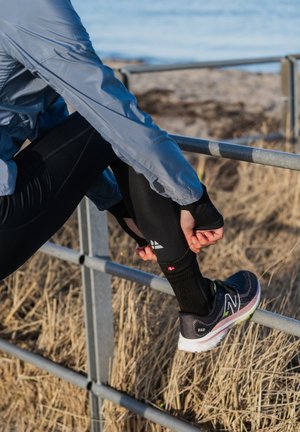 Lekka szara kurtka, czarne legginsy i czarne buty sportowe z różowymi akcentami. Posiada odblaskowe detale i wzorzystą skarpetkę.