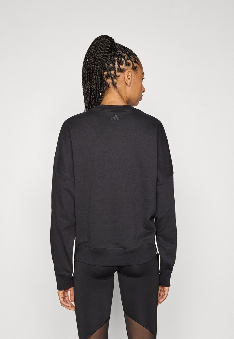 Sweat-shirt noir à col rond et manches longues, avec un logo discret au dos. Le tissu semble lisse et sportif.
