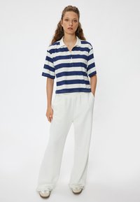 Navy ja valge triibuline polo särk kraega, kombineeritud lõtvade valgete dressipükste ja beežide libistatavate kingadega.