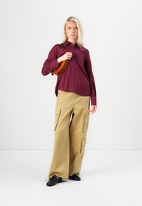 Burgundy button-up shirt with a relaxed fit, paired with tan cargo pants featuring multiple pockets and a wide leg. Black shoes complete the outfit.