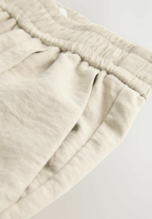 Pantalons de jogging en coton beige clair avec une taille élastique et un tissu doux et texturé, ornés de détails froncés au niveau de la taille.
