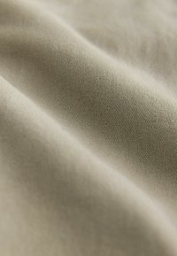 Nærbillede af beige stof med fin vævet tekstur og bløde folder, som skaber bløde skygger.