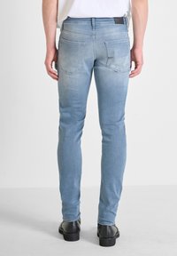 Svijetloplave uske traperice s izblijedjelim opranjem, s dvije stražnje džepove i malom crnom etiketom na remenu. Glatka denim tekstura.