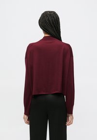 Pulover burgund în croială scurtă cu mâneci lungi, finisaj texturat, spate decupat și croială lejeră, asortat cu pantaloni negri cu talie înaltă.