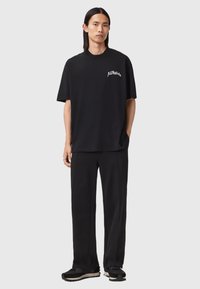 Sort T-shirt med korte ærmer, afslappet pasform, med lille hvidt logo på venstre bryst. Fremstillet af blød bomuld. Kombineret med sorte bukser og sko.