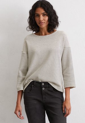 Long-sleeve, striped top in beige and black, featuring a wide neckline and relaxed fit. Paired with black jeans for a casual look.