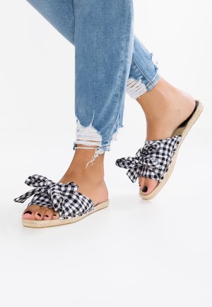 Sandales à enfiler en vichy noir et blanc avec de grands nœuds, semelle en jute et bout ouvert. Portées avec un jean bleu clair déchiré.