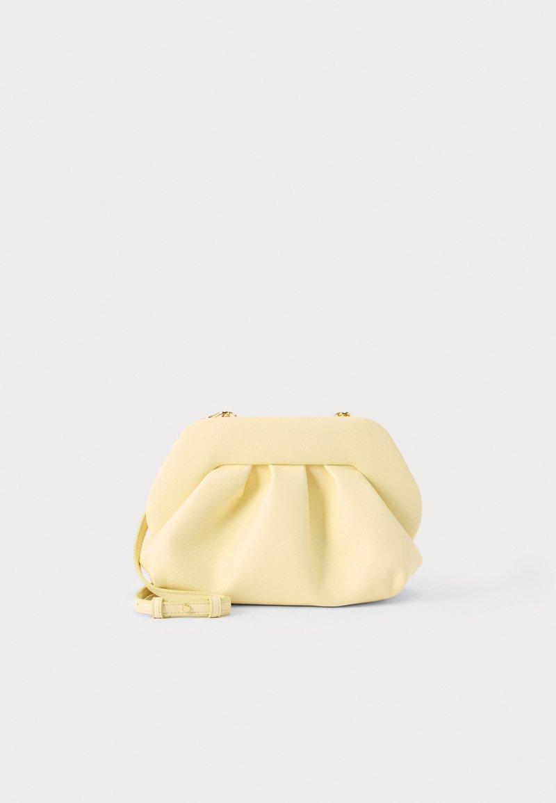 Pochette en cuir jaune doux avec un design froncé et une bandoulière amovible, posée sur un fond clair uni.