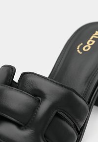 Schwarze Leder-Sandale mit Schlupfdesign, gepolsterter Ausführung und rechteckigen Ausschnitten. Das goldene „ALDO“-Logo auf der Innensohle setzt einen dezenten Akzent.