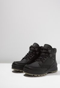 Botas de senderismo negras hechas de cuero y tela, con un diseño de cordones, cuello acolchado y una suela de goma robusta con acentos texturizados.