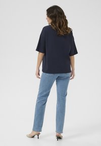 T-shirt oversized bleu marine à manches courtes, associé à un jean droit bleu clair et des sandales à talons beiges. Design simple avec une coupe décontractée.
