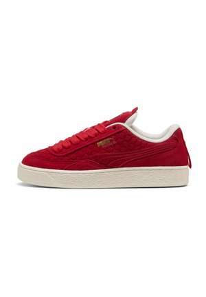 Zapatilla de ante rojo con un patrón de diamantes texturizado, suela de goma blanca y cordones a juego. Incluye una pequeña lengüeta en el talón para facilitar el calce.