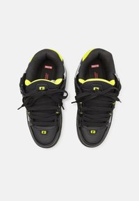 Black sneakers with yellow accents and silver detailing. Features a smooth texture, traditional lace-up design, and padded collar.