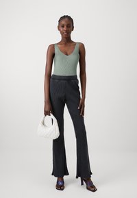 Randig grön bodysuit, svarta utsvängda byxor med ränder, vit vadderad handväska och lila klacksandaler. Modellen står vänd framåt.