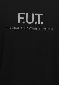 Svart t-shirt med texten "F.U.T." i fet vita bokstäver ovanför "FYSISK UTVECKLING & TRÄNING", med en mjuk bomullstextur.