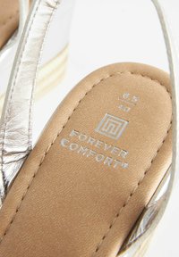 Hnědá stélka s texturovaným povrchem, stříbrný řemínek a vytlačené logo "FOREVER COMFORT" ve stříbrné barvě. Velikost 6,5/40 je uvedena na stélce.