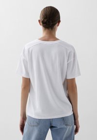Witte katoenen t-shirt met korte mouwen, ronde hals en een ontspannen pasvorm. Glad textuur, met een eenvoudig ontwerp aan de achterkant.