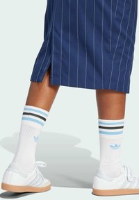 Vita atletiska skor med en texturerad gummisula, i kombination med knähöga vita strumpor med blå och svarta ränder, bärs med en marinblå randig kjol.