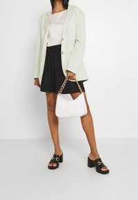 Miętowo zielona marynarka, beżowa bluzka, czarna spódnica i czarne platformowe klapki. Biała torebka z złotym łańcuszkiem, z ozdobnym fakturowanym detalem.