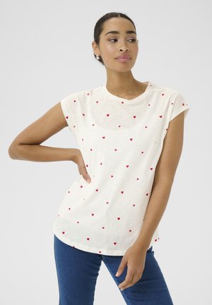 T-shirt crème à manches courtes avec un motif de cœurs rouges dispersés, col rond et coupe décontractée, associé à un jeans en denim bleu.