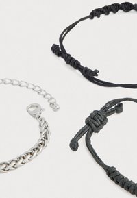 Trīs aproces: sudraba ķēdes aproce, melnā aušanas auklas aproce un mezglota melna virves aproce ar regulējamām aizdarēm.