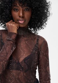 Brązowa przezroczysta bluzka z wzorem skóry węża; wysoki kołnierz; długie rękawy; jednowarstwowy materiał odsłaniający czarną bieliznę.
