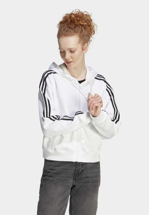 Sudadera blanca con cremallera y rayas negras en los hombros, con capucha ajustable. Cuenta con un corte relajado, tela suave y bolsillos frontales, combinada con jeans oscuros.
