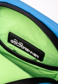 L'intérieur du sac bleu et noir est doté d'une doublure verte vif, avec une étiquette noire portant "CLO GOLDBRENNER" en lettres blanches. Ouverture zippée.