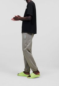 Černé tričko s krátkým rukávem, světle šedé tepláky s elastickými manžetami a jasně zelené pantofle. Jednoduchý design s detailním logem na kalhotách.