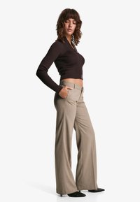 Hnědý žebrovaný top s dlouhými rukávy a zkráceným střihem, doplněný světlými béžovými širokými kalhotami a černými lodičkami s špičatou špičkou.