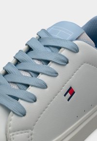 Λευκό αθλητικό παπούτσι με μπλε κορδόνια και γλώσσα ανοιχτού μπλε χρώματος. Διαθέτει μικρό λογότυπο σε κόκκινο, λευκό και μπλε, με διάτρητες λεπτομέρειες στην πλευρά.