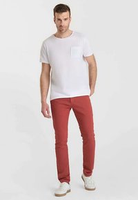 Vit kortärmad t-shirt med bröstficka kombinerad med röda slim fit-byxor och vita sneakers, mot en neutral bakgrund.